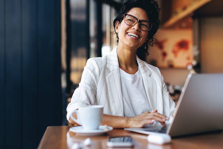 Woman smiling while working on a laptop in a cafe